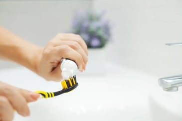 A person brushes their teeth with a yellow and black toothbrush, highlighting the importance of oral hygiene in teledentistry